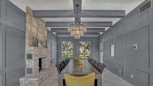 Un comedor amplio con una larga mesa y sillas amarillas, una chimenea de piedra y ventanas grandes con vistas a la vegetación.