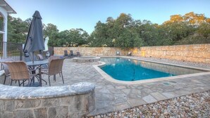 Una piscina rectangular con borde de piedra, rodeada de escalones de piedra y una zona de estar con sillas y una mesa.