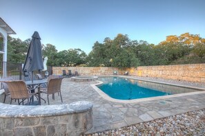 A rectangular swimming pool with a stone border, surrounded by stone steps and a seating area with chairs and a table.
