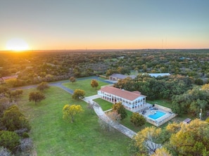 An aerial view of a large estate with a prominent building, a swimming pool, and surrounding greenery.