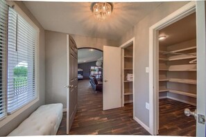 A hallway with a bench, a closet with shelves, and a door leading to a room with a bed and a chair. - New Braunfels Estate, Two Homes, Pool + Sleeps 34 (New Braunfels)
