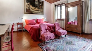 Quarto com cama, duas cadeiras, penteadeira, espelho e quadro na parede.