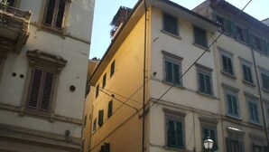 Um edifício de vários andares com fachada amarela, várias janelas com persianas e um poste de luz fixado na fachada.