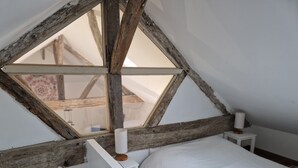 A bedroom with a sloped ceiling, a wooden beam structure, a bed, and a nightstand with a lamp. - The Wine Press (Turquant)