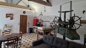 A rustic kitchen with a large wooden beam ceiling, a red refrigerator, and a vintage mechanical device. - The Wine Press (Turquant)
