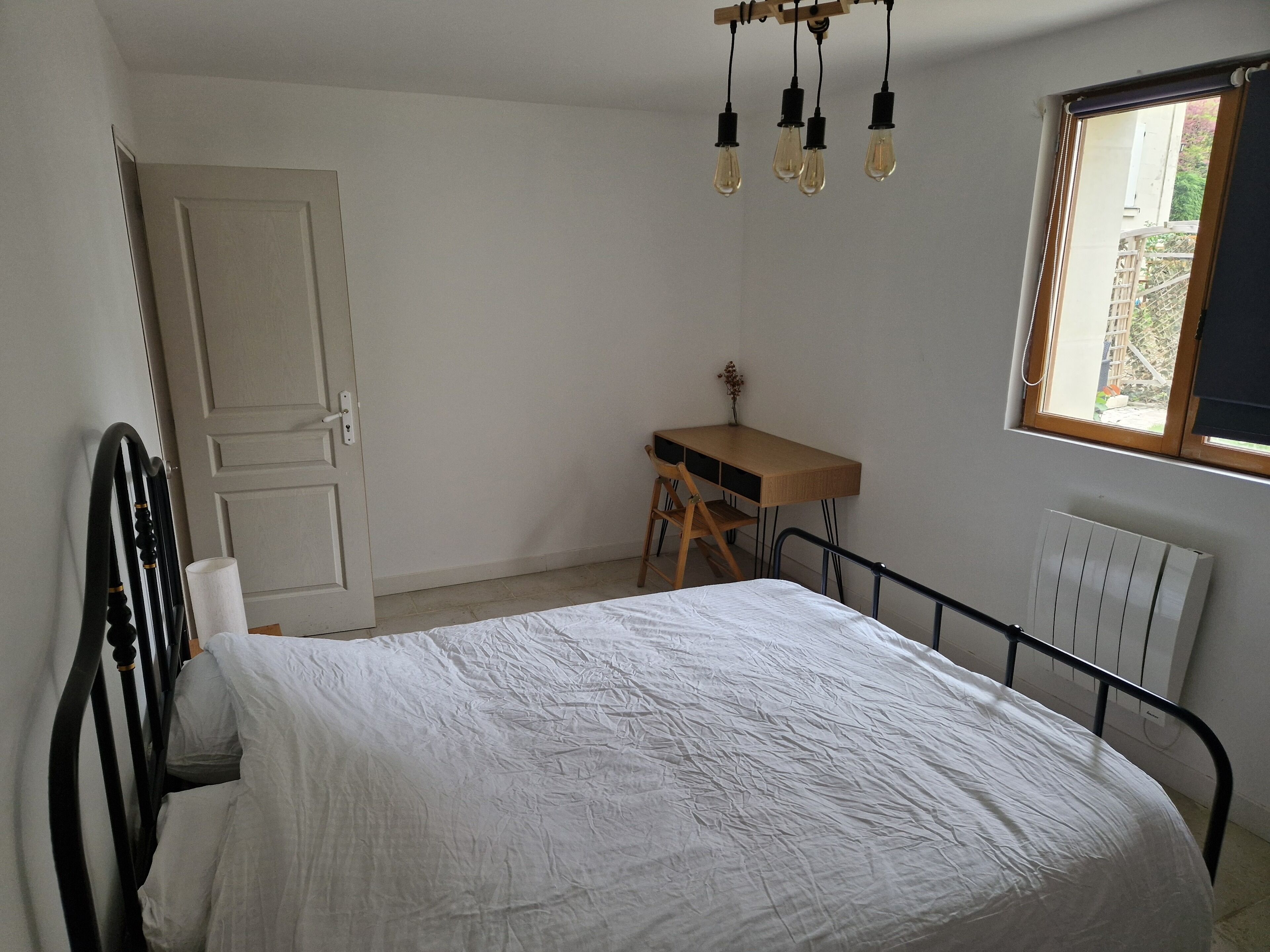 A bedroom with a bed, a desk, and a window.