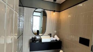 Een moderne badkamer met een douchecabine van glas, een zwart wastafelmeubel met een spiegel en een wit toilet.