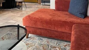 Een moderne hotelkamer met een rode bank, een glazen bijzettafeltje, een bed met een geel hoofdeinde en een eethoek met een zwarte tafel en stoelen.