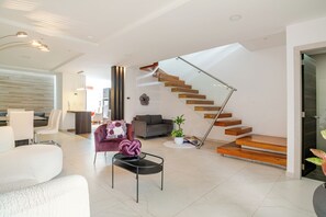 Un salon moderne avec un escalier, un canapé, une table basse et un coin repas.