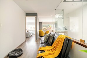 Un salon moderne avec un canapé en cuir, un plaid jaune et une table basse en verre.