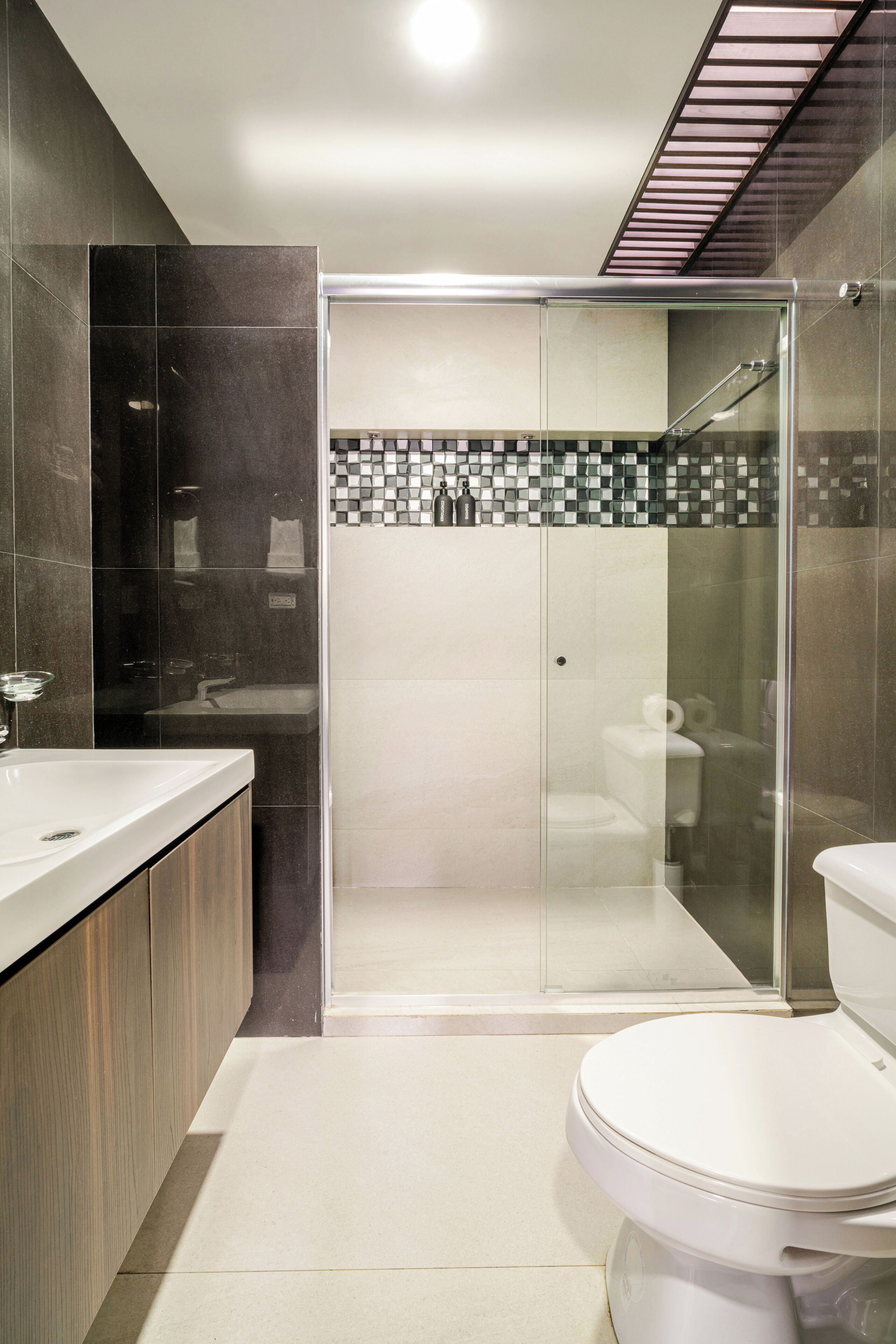 Ein modernes Badezimmer mit einer einteiligen Glasdusche, einer weißen Toilette und einem Waschtisch mit Spiegel.