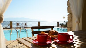 Un tavolino a bordo piscina con due bicchieri rossi e un pasticcino, con vista sulla piscina e un cielo sereno.