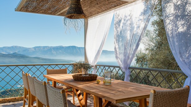 Un tavolo di legno con sedie in vimini, un cesto e una brocca d'acqua, con una vista panoramica sulle montagne.