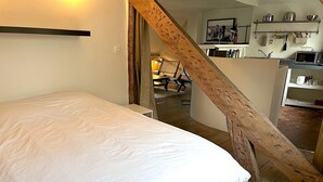 A bedroom with a large bed, wooden staircase, and a kitchen area visible in the background. - Le Penthouse Picardie (Paris)