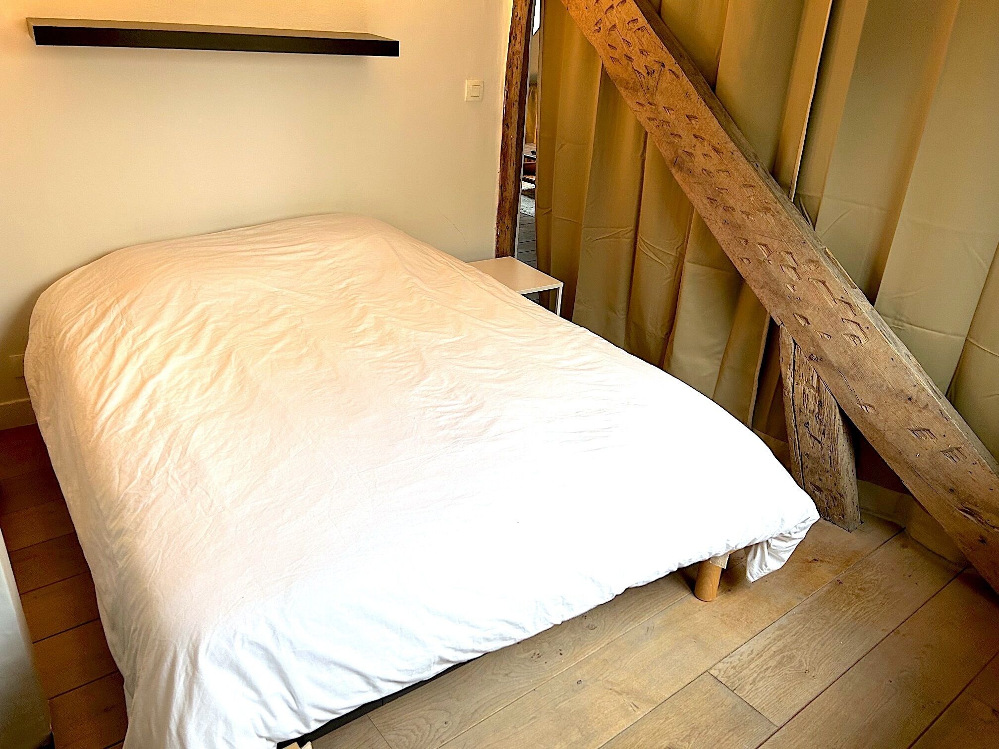 A single bed with a white mattress in a room with wooden flooring and a wooden staircase.