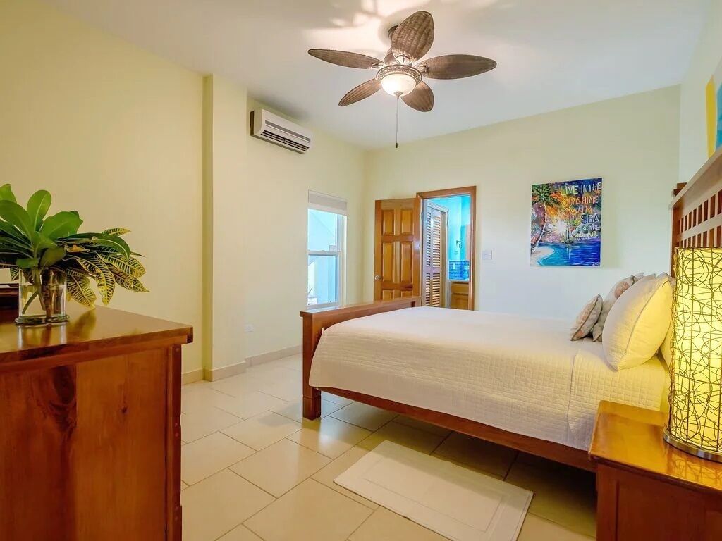 A bedroom with a wooden bed, a ceiling fan, a window, and a painting on the wall.