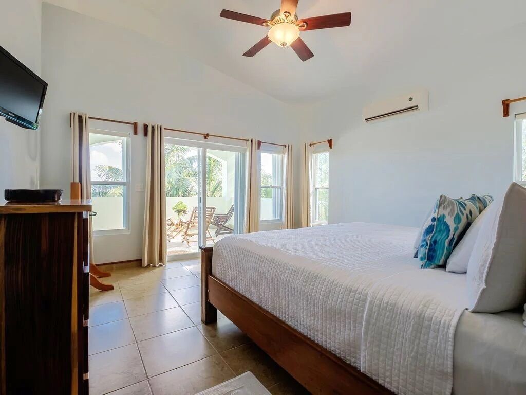 A bedroom with a bed, a ceiling fan, a television, and a sliding glass door leading to an outdoor area.