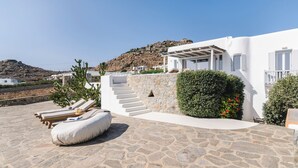 Uma vila branca com um alpendre de pedra, área de estar externa e vista para uma encosta rochosa.