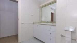 Ein Badezimmer mit weißen Fliesen, einem weißen Waschtisch und einem Spiegel sowie einer Toilette.