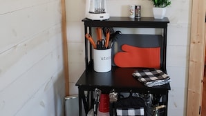 Una cocina con cafetera, tazas colgando, una planta y varios utensilios de cocina sobre un estante negro.