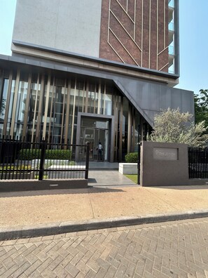 Un bâtiment moderne doté d’une entrée imposante, d’une allée bordée de portails et d’un espace paysager agrémenté d’arbustes.