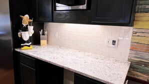 A kitchen with black cabinets, a white tiled backsplash, and a granite countertop. - Home Near USC, Perfect for Families & Graduations - Deja Blues  (West Columbia)