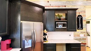 A modern kitchen with dark cabinetry, a stainless steel refrigerator, a microwave, and a welcome sign. - Home Near USC, Perfect for Families & Graduations - Deja Blues  (West Columbia)