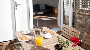 An outdoor dining area with a wooden table, chairs, and a potted plant. - Contemporary cottage in lovely Devon village. (Musbury)