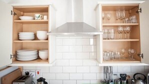 A kitchen with white cabinets, a central range hood, and a tiled backsplash. - Contemporary cottage in lovely Devon village. (Musbury)
