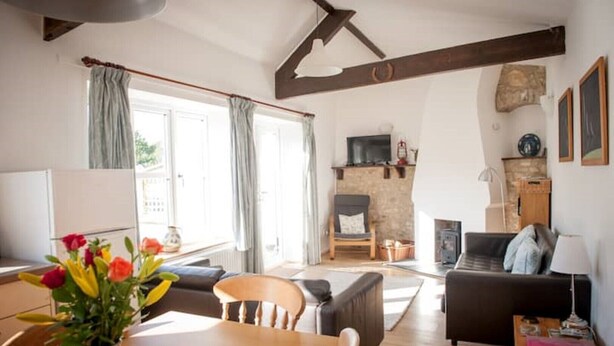 A spacious living area with a fireplace, a dining table with chairs, a sofa, and a TV. - Contemporary cottage in lovely Devon village. (Musbury)