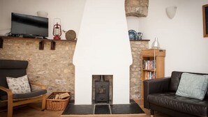 A cozy living room with a stone wall, a fireplace, a television, and a bookshelf. - Contemporary cottage in lovely Devon village. (Musbury)