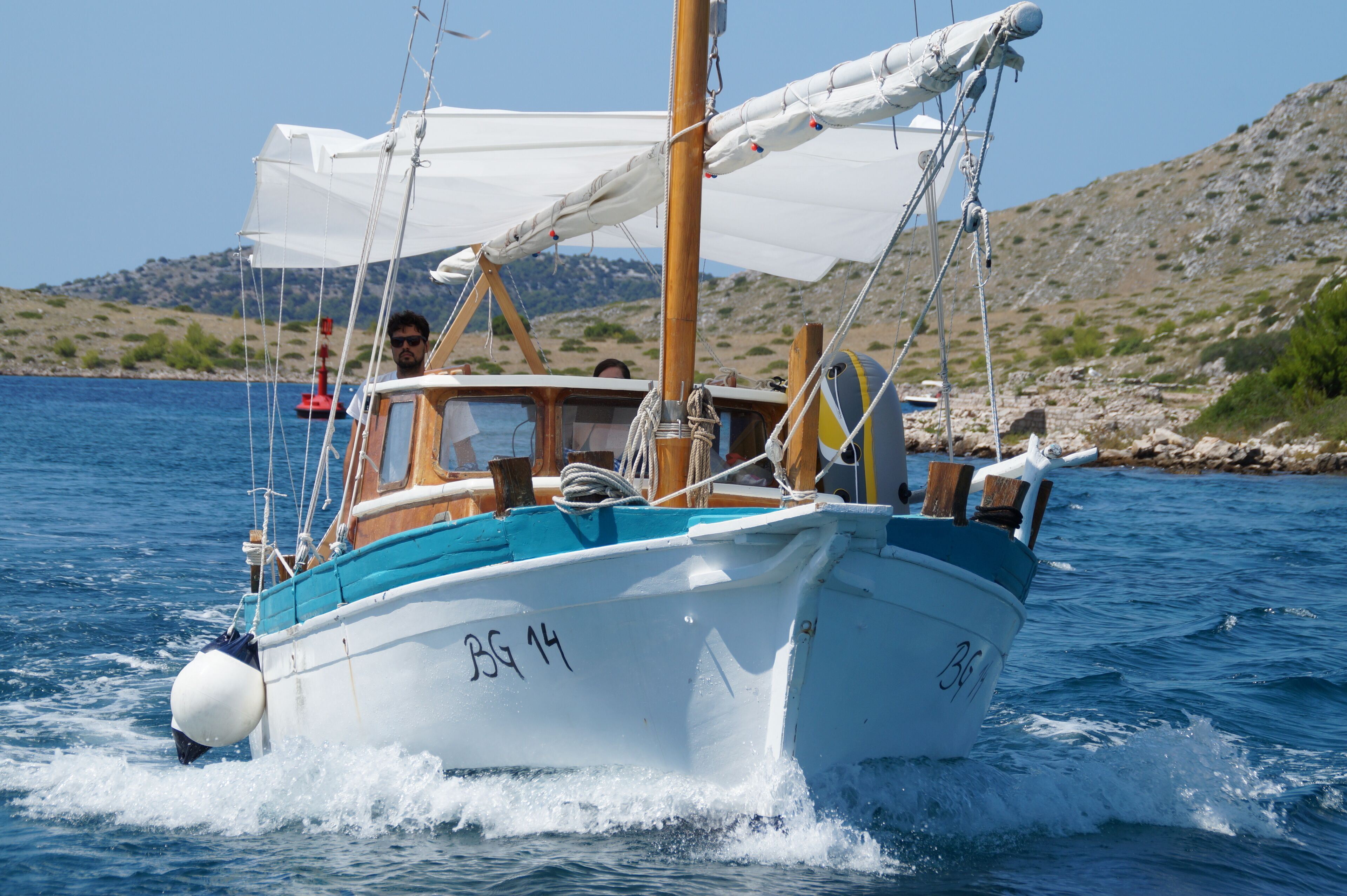 A boat with the number 'BG 14' on its side, sailing on a body of water with a rocky shoreline in the background.