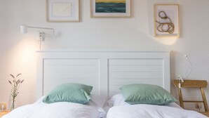 Ein Schlafzimmer mit einem weißen Kopfteil, zwei grünen Kissen, einem Nachttisch mit Lampe und gerahmten Bildern an der Wand.