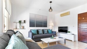 Una sala de estar moderna con un sofá gris, un sofá azul, una mesa de centro blanca, un televisor y una puerta de madera.