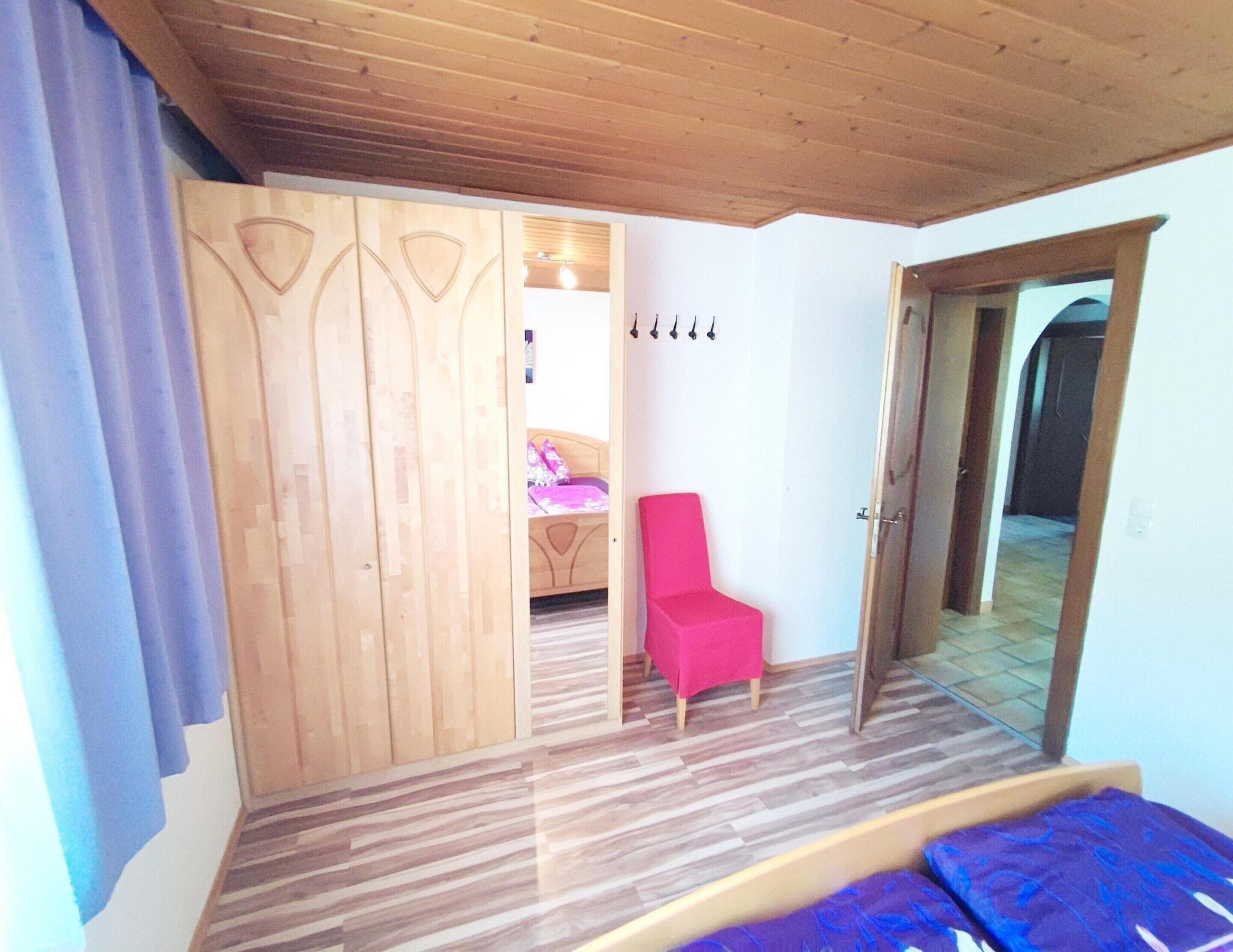 A room with a bed, a red chair, and a wooden wardrobe.