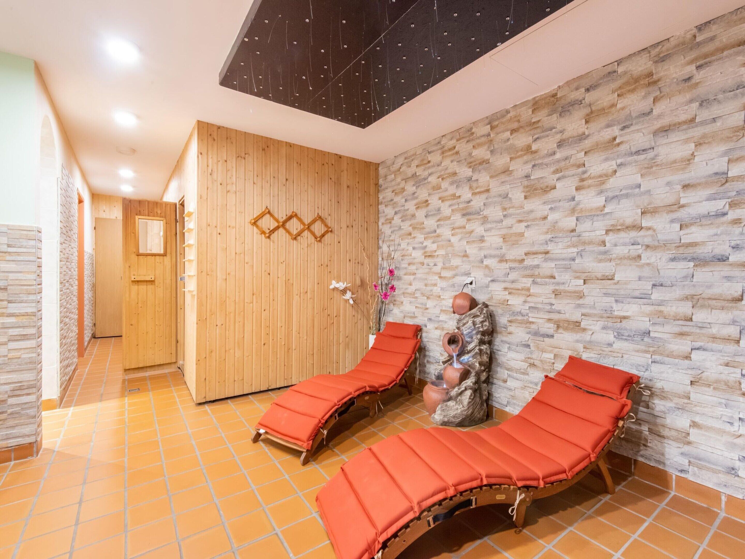 A spa room with wooden walls, a stone wall, and two red lounge chairs.