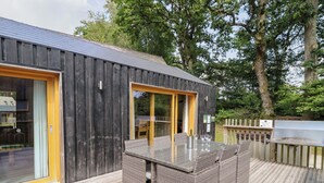 Un bâtiment moderne en bois, doté d’une porte et de fenêtres en verre, d’une terrasse avec des meubles en osier et d’un panneau indiquant qu’il s’agit d’un espace privé.