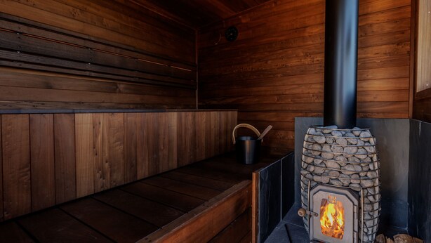 Un intérieur en bois avec une cheminée en pierre, un banc et un pot suspendu au mur.