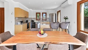 A modern kitchen with wooden cabinets, a central island, and a dining area with a large wooden table and cushioned chairs. - Villa TA01 Ouranos - Three Bedroom Villa, Sleeps 6 (Kouklia)