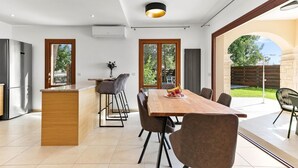 A modern kitchen with a large island, dining area with chairs, and a view of the outdoors. - Villa TA01 Ouranos - Three Bedroom Villa, Sleeps 6 (Kouklia)