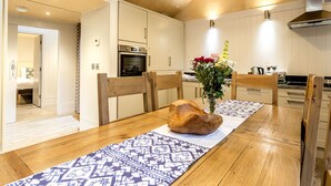 A modern kitchen with wooden cabinets, a central island, and a dining area with a patterned rug. - Lodge 13 (Wareham)