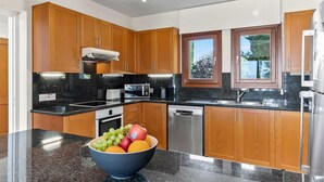 Een moderne keuken met houten kasten, granieten aanrecht en roestvrijstalen apparatuur, met een schaal fruit op het aanrecht.