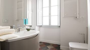 A bathroom with a white sink, a mirror, a window with shutters, a toilet, and a patterned floor.