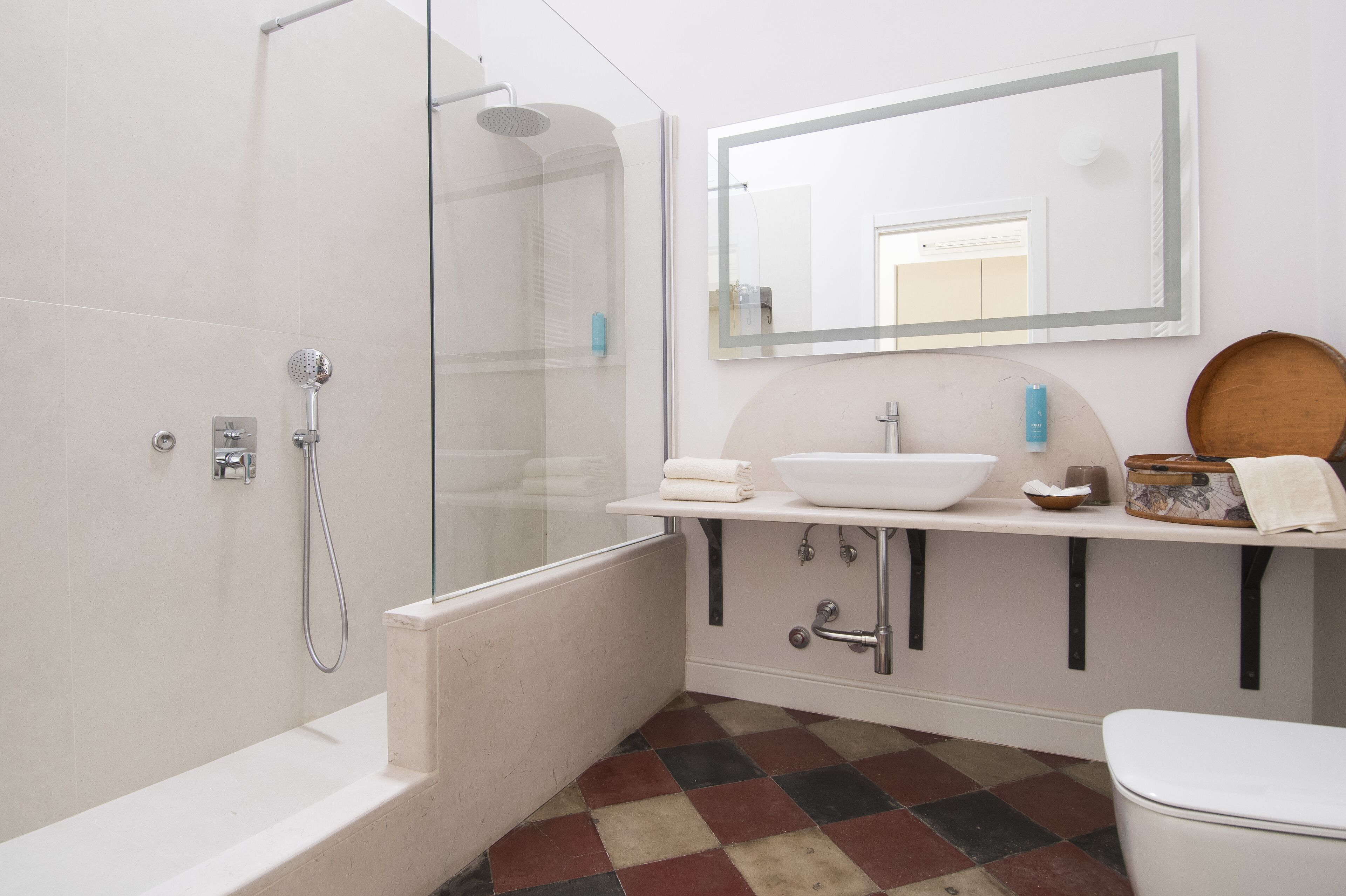 A bathroom with a glass-enclosed shower, a white sink with a bowl, a mirror, and a checkered floor.