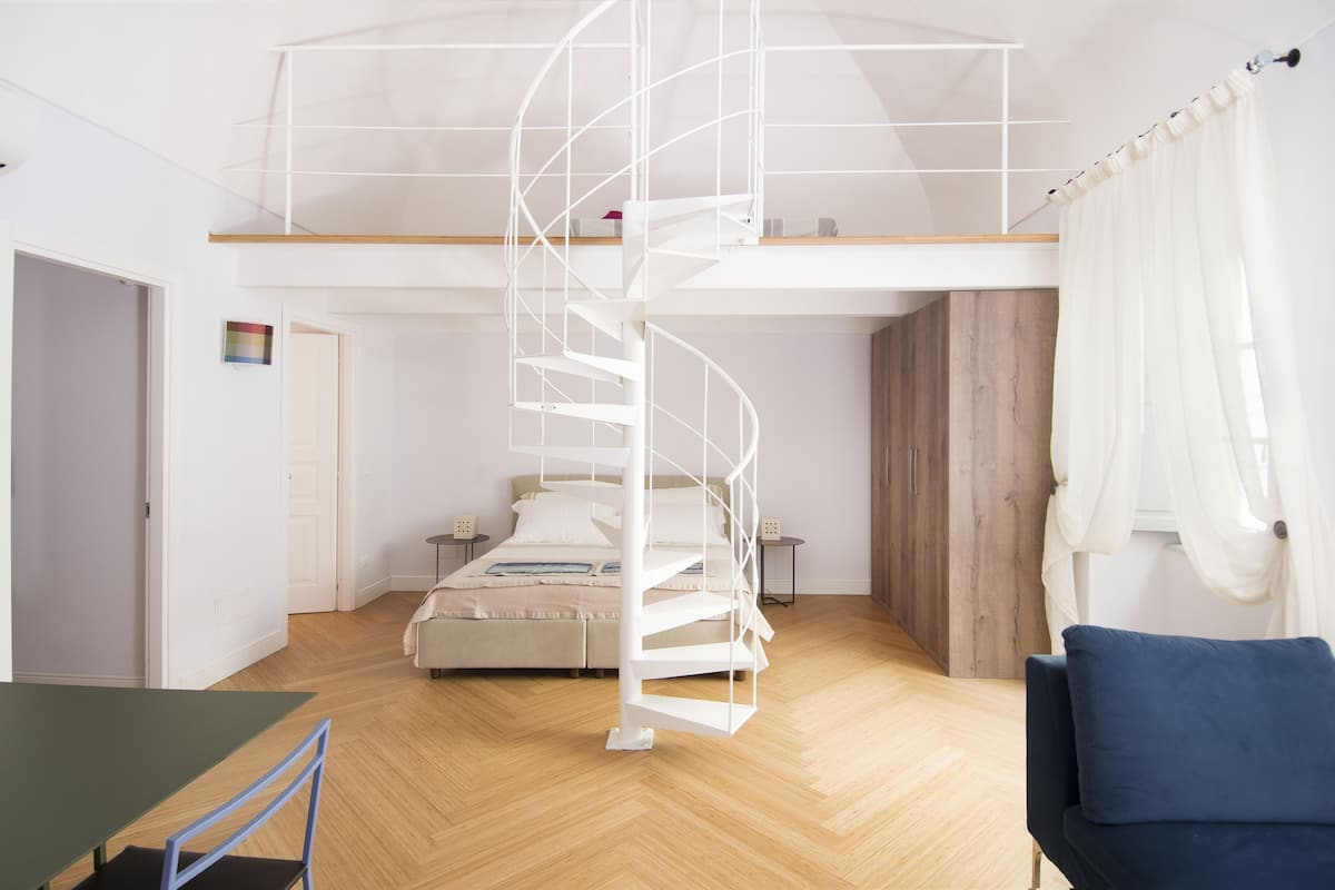 A modern bedroom with a spiral staircase, a bed, a nightstand, and a wooden wardrobe.