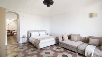 Une chambre à coucher avec un lit, un canapé et une petite table. Un escalier mène à une autre pièce.