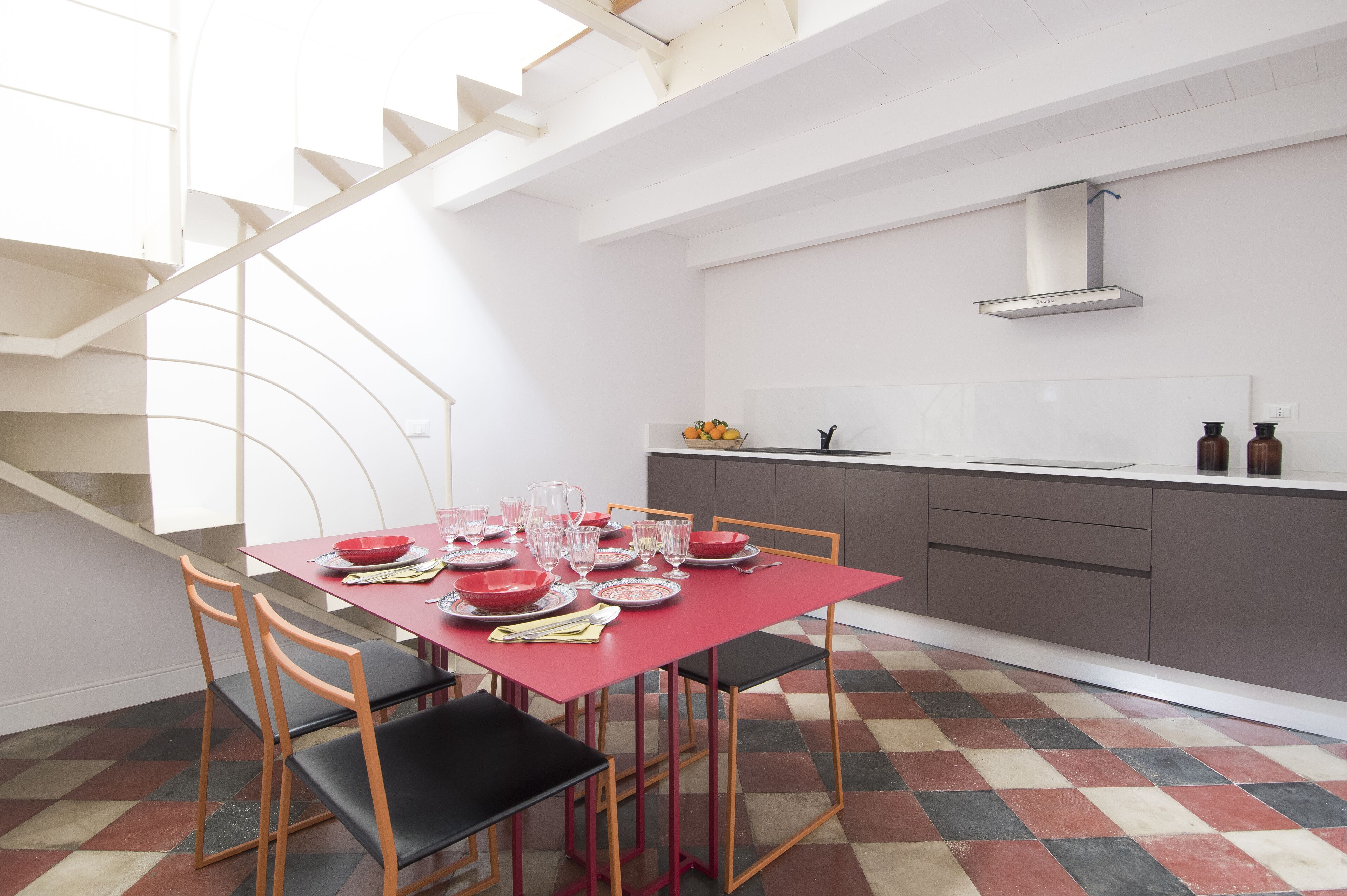 Una cocina moderna con una mesa de comedor roja para seis personas, una escalera y vistas al exterior.