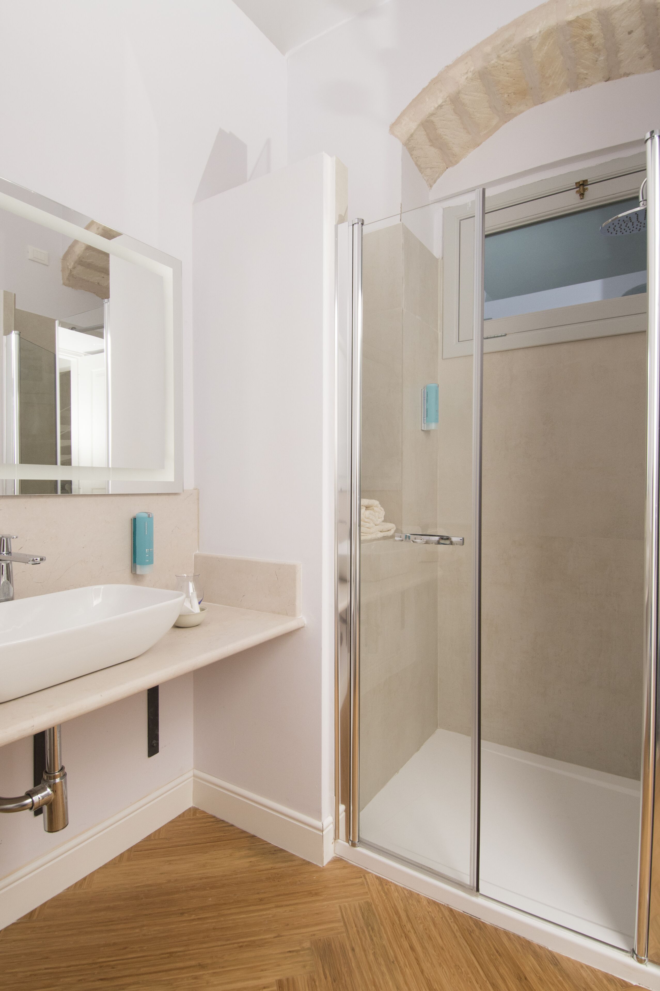 Un baño con un lavabo blanco, una cabina de ducha de vidrio y un espejo sobre el lavabo.