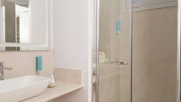 Un baño con un lavabo blanco, una cabina de ducha de vidrio y un espejo sobre el lavabo.