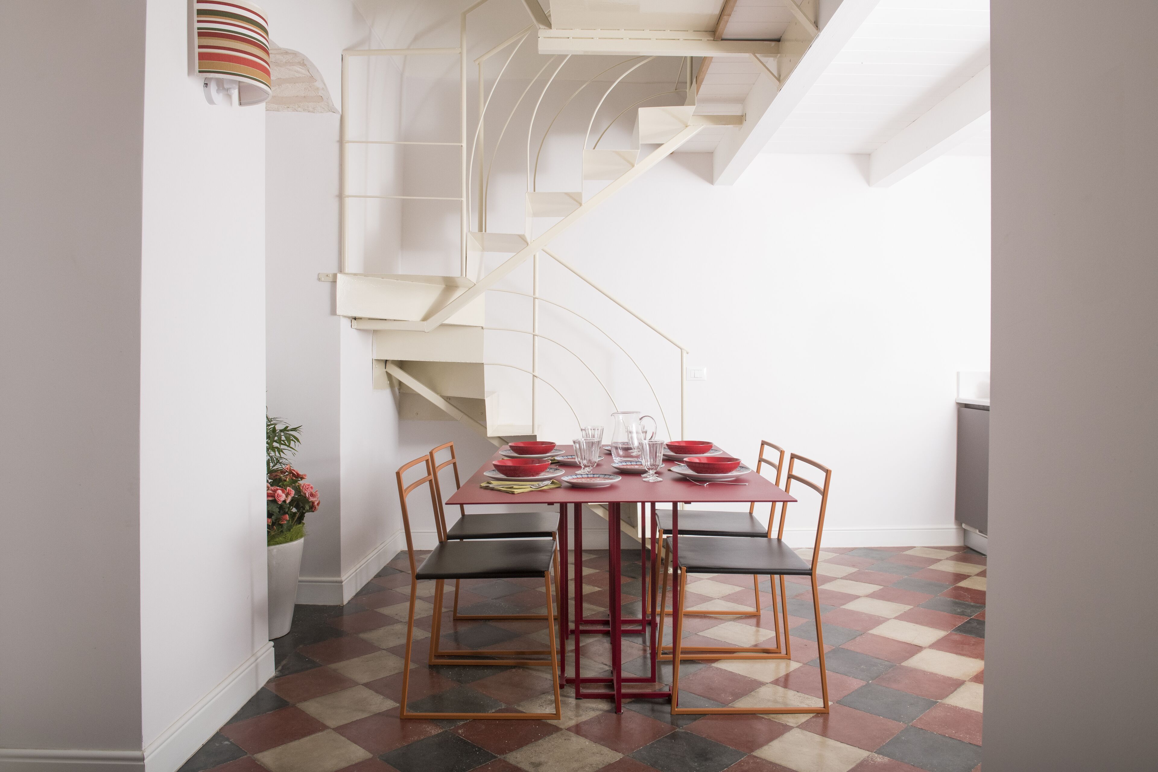 A dining area with a red table, black chairs, and a checkered floor.